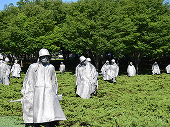 There are statues of soldiers that look like they are walking through a field. They are shown wearing battle clothes including helmets, raincoats, and guns.