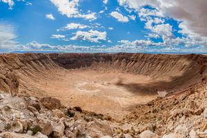 A crater in the desert is shaped like a bowl and has large cliffs.