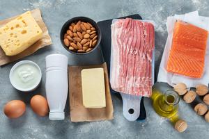 Eggs, cheese, cream, salmon, almonds, butter, bacon, oil, and walnuts on a countertop.