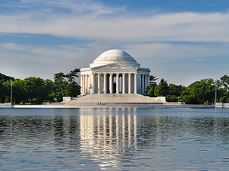 This is a white, circular building. It has many columns and a small dome on top.The building is on the edge of a river.