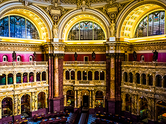 This is a circular room. The walls are made up of pillars, arches, and statues. On the floor there are many tables.