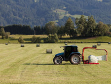 There is a tractor harvesting hay in a field. There are no buildings nearby.