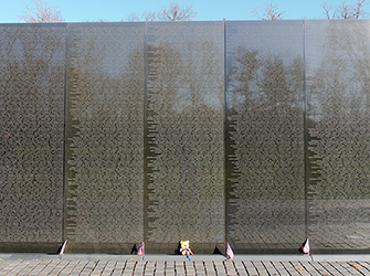 This is a large, black wall that looks like a mirror. There are names carved into the wall and small American flags at the base of the wall.