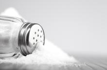 White crystals pouring out of a salt shaker onto a table.